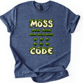 Moss Code Comfort Colors T-shirt in Heather Navy, laid flat. Cream bubble letters reading MOSS and CODE are overgrown with green moss, with rows of moss-covered Morse code dashes and dots between them. The shirt has rolled sleeves on a white background.