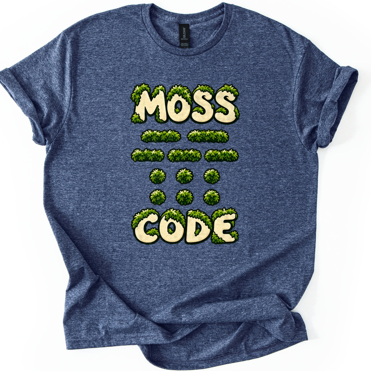 Moss Code Comfort Colors T-shirt in Heather Navy, laid flat. Cream bubble letters reading MOSS and CODE are overgrown with green moss, with rows of moss-covered Morse code dashes and dots between them. The shirt has rolled sleeves on a white background.