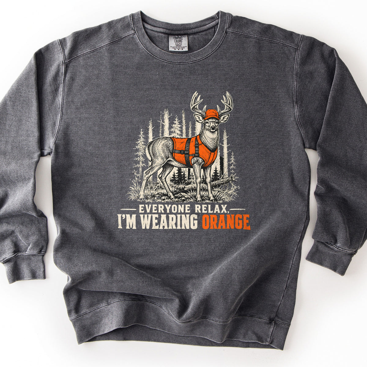 Everyone Relax, I'm Wearing Orange Comfort Colors crewneck sweatshirt in Pepper, laid flat. A sketched whitetail buck in an orange hunting vest and orange cap stands in a pine forest above the words Everyone Relax, I'm Wearing Orange, with Orange in orange. Shown on a white background.