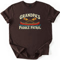 Grandpas Paddle Patrol Comfort Colors T-shirt in Dark Chocolate, laid flat. Cream lettering reads Grandpa's above two crossed wooden paddles with a small red heart and a red canoe on blue water, with Paddle Patrol below. The shirt lies on a white background with sleeves rolled.