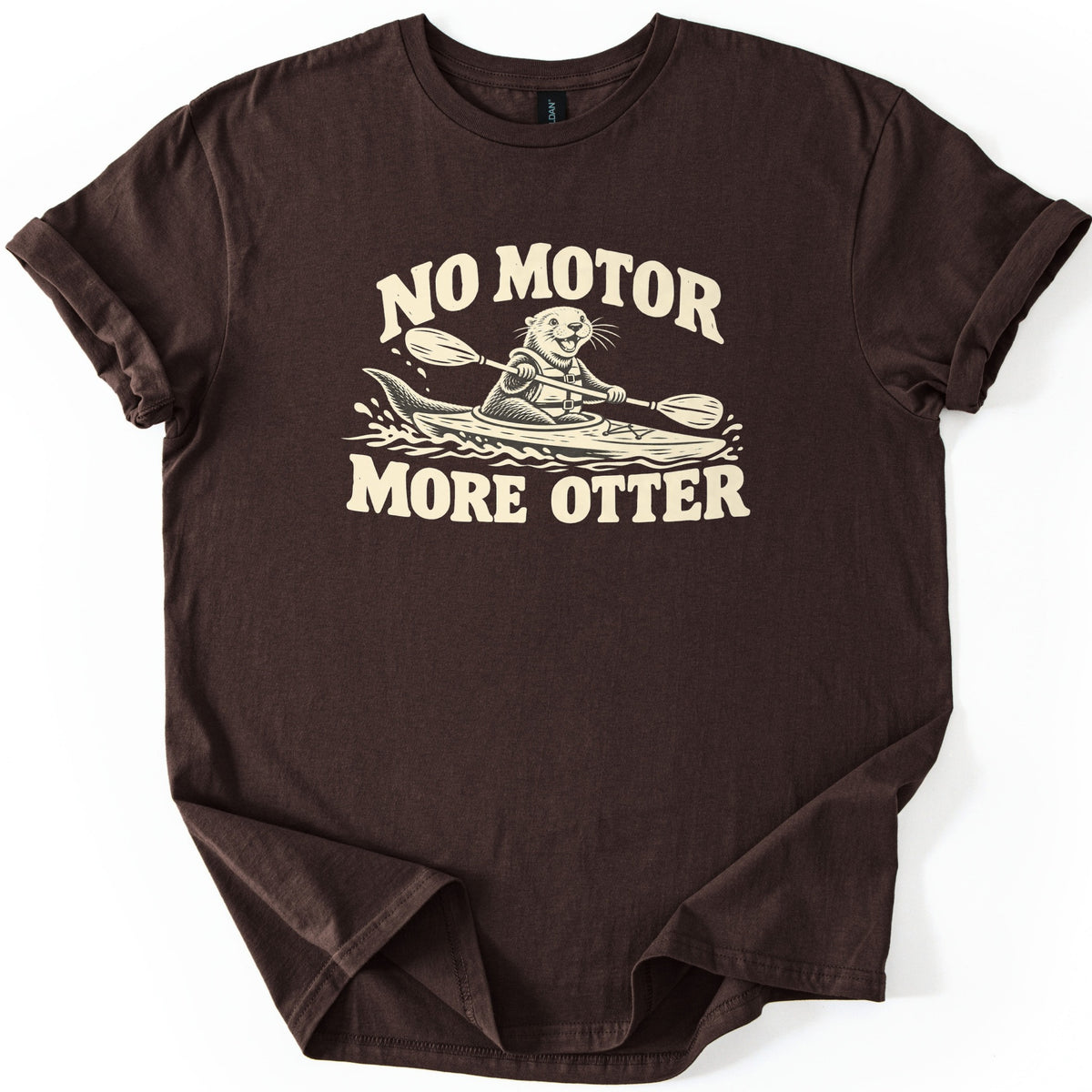 No Motor More Otter Comfort Colors T-shirt in Dark Chocolate, laid flat. A cream print of a smiling otter in a life vest paddling a kayak through splashing water, with NO MOTOR arched above and MORE OTTER below. The shirt has cuffed sleeves on a white background.
