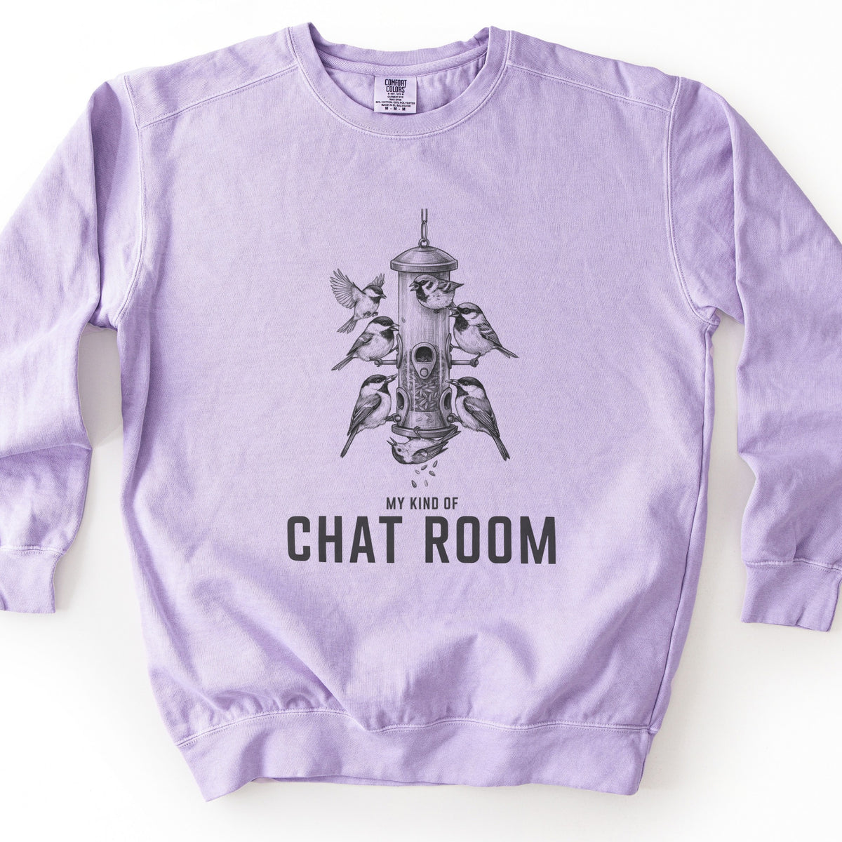 My Kind Of Chat Room Comfort Colors crewneck sweatshirt in Orchid, laid flat. A charcoal sketch of chickadees perched around a hanging tube bird feeder, one in flight and one upside down below with seeds falling, above the words MY KIND OF CHAT ROOM. Shown on a white surface.