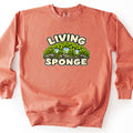 Living Sponge Comfort Colors crewneck sweatshirt in Terracotta, laid flat. The front shows a mound of bright green moss on gray rock holding three clear water droplets, with the words Living Sponge in cream bubble letters above and below. It lies on a white background.