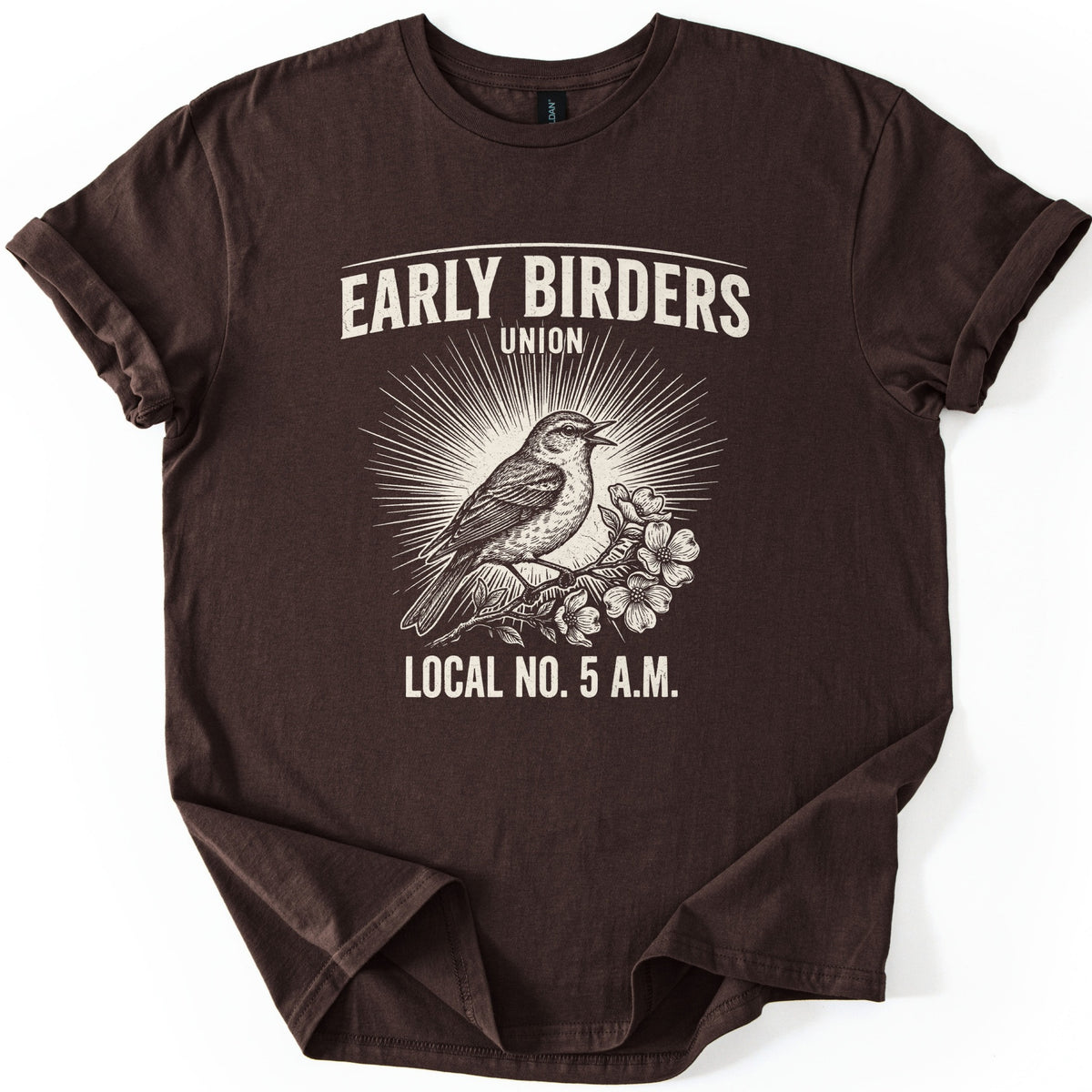 Early Birders Union Comfort Colors T-shirt in Dark Chocolate, laid flat. A cream vintage-style engraving of a songbird singing on a flowering branch before sunburst rays, with Early Birders Union above and Local No. 5 A.M. below. The shirt lies on a white background with rolled sleeves.