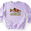 Dressed for the Current Comfort Colors crewneck sweatshirt in Orchid, laid flat. A spotted trout wearing a red knit holiday sweater with a tree and snowflake pattern leaps through splashing water above the words Dressed for the Current. Laid on a white background.