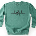 Snow Boarder Heartbeat Comfort Colors crewneck sweatshirt in Light Green, laid flat. A black heartbeat line runs across the chest, rising into a mountain peak with a snowboarder riding on top and small dots of snow around it. No words. The sweatshirt lies on a white surface.