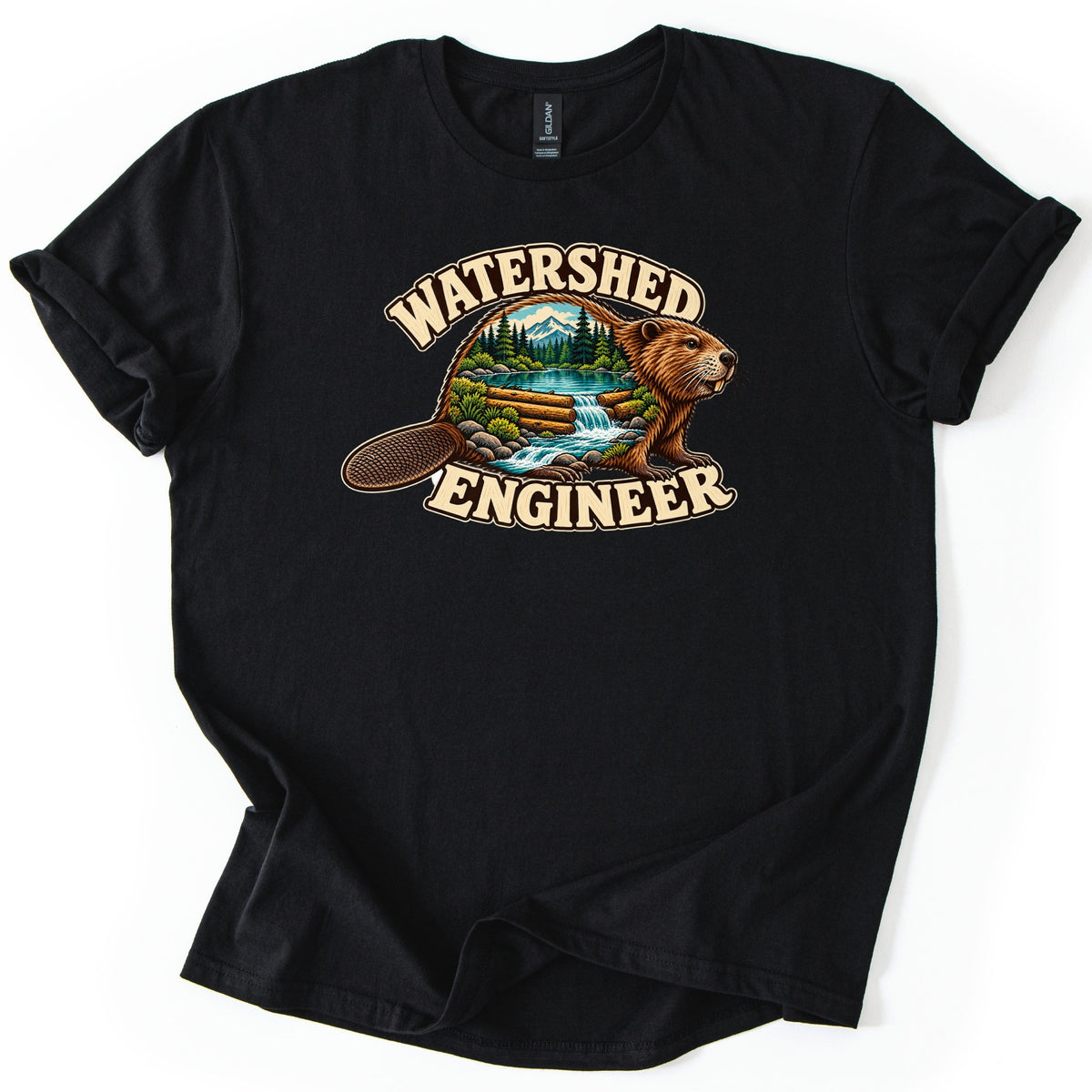 Watershed Engineer Comfort Colors T-shirt in Black, laid flat. A beaver whose body frames a scene of a snowy mountain, pine trees, a lake, and a log dam with a waterfall, between the words Watershed Engineer. The sleeves are rolled, on a white background.