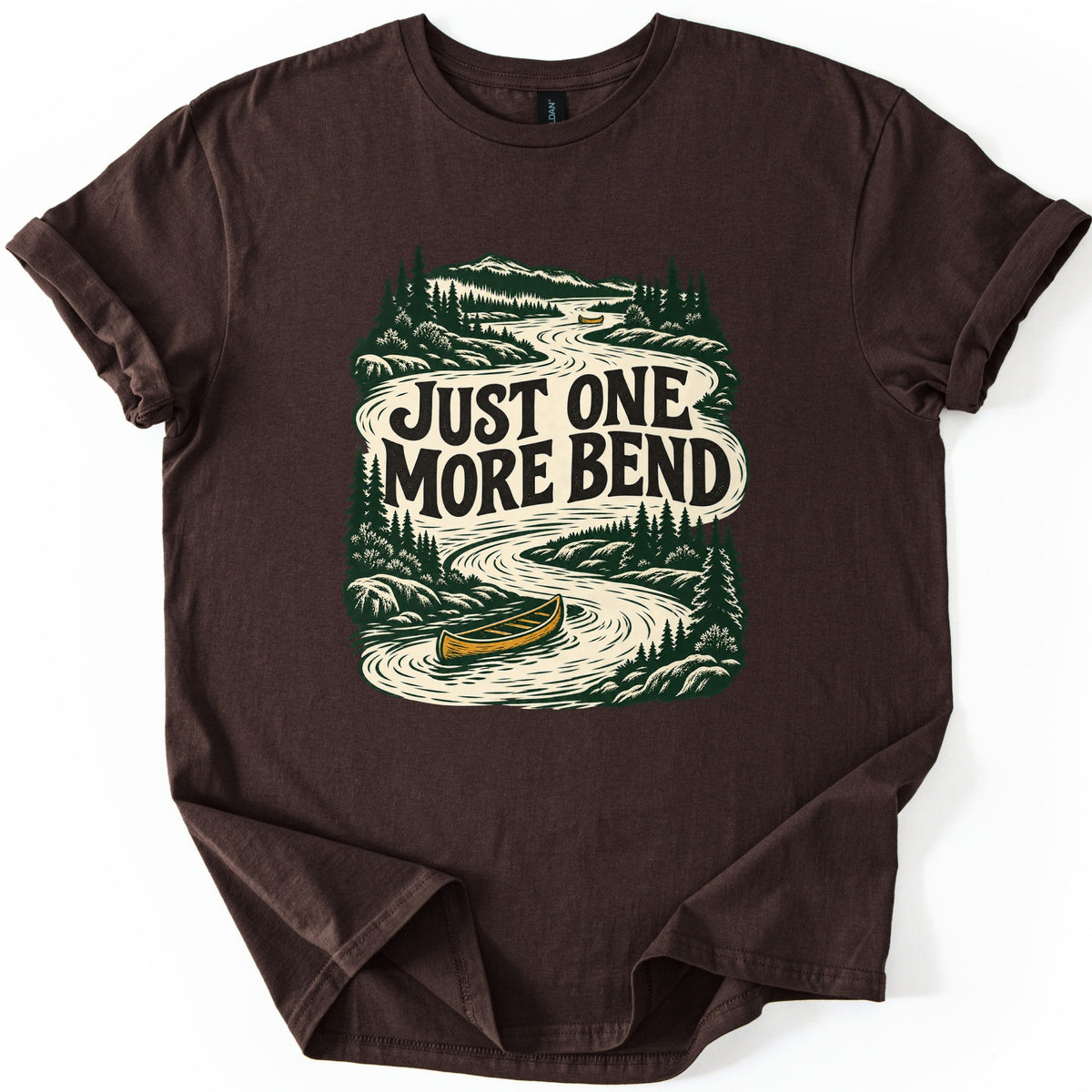 One More Bend Comfort Colors T-shirt in Dark Chocolate, laid flat. A woodcut-style print of a winding river through pine forest and mountains, with a yellow canoe in front and another far upstream, and the words Just One More Bend across the water. Sleeves rolled, on white.