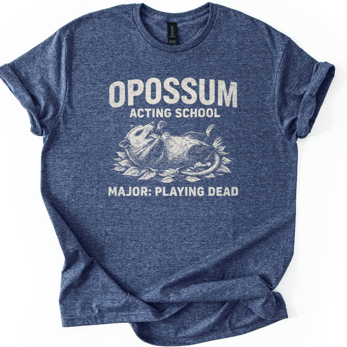 Opossum Acting School Comfort Colors T-shirt in Heather Navy, laid flat. A cream sketch of an opossum lying on its back on a bed of leaves, mouth open, sits under the words OPOSSUM ACTING SCHOOL and above MAJOR: PLAYING DEAD. The sleeves are rolled on a white background.