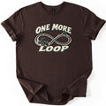 One More Loop Comfort Colors T-shirt in Dark Chocolate, laid flat. A helmeted rider on an ATV kicks up dirt along an infinity-shaped tire track with pine trees, between the words One More Loop in cream letters. The shirt has cuffed sleeves on a white background.