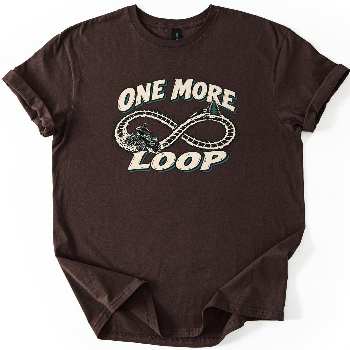 One More Loop Comfort Colors T-shirt in Dark Chocolate, laid flat. A helmeted rider on an ATV kicks up dirt along an infinity-shaped tire track with pine trees, between the words One More Loop in cream letters. The shirt has cuffed sleeves on a white background.