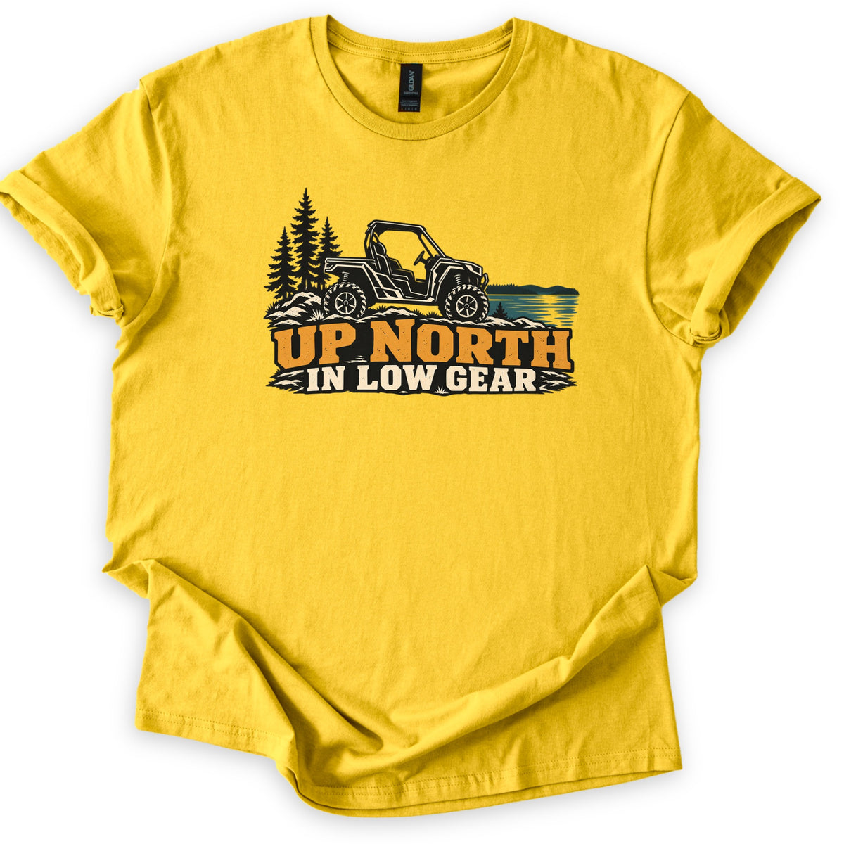 Up North in Low Gear Comfort Colors T-shirt in Daisy, laid flat. A black side-by-side UTV on rocky ground between pine trees and a blue lake sits above the words UP NORTH in orange and IN LOW GEAR in cream. The shirt has cuffed sleeves on a white background.