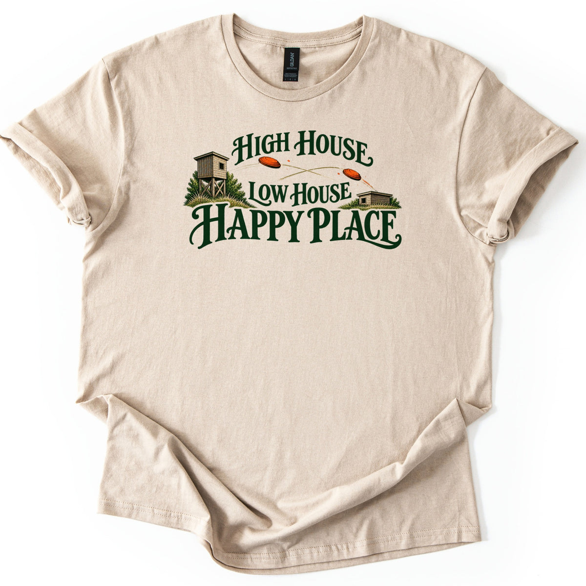 High House Low House Happy Place Comfort Colors T-shirt in Sand, laid flat. A wooden skeet high house tower and low house sit in grass with orange clay targets flying between them, around dark green words High House Low House Happy Place. Sleeves are cuffed on a white background.