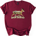 Made for Open Country Comfort Colors T-shirt in Maroon, laid flat. A walking pronghorn whose body is filled with a desert scene of mesas, sagebrush and a dirt trail sits above the words Made for Open Country. The shirt lies on a white surface with cuffed sleeves.