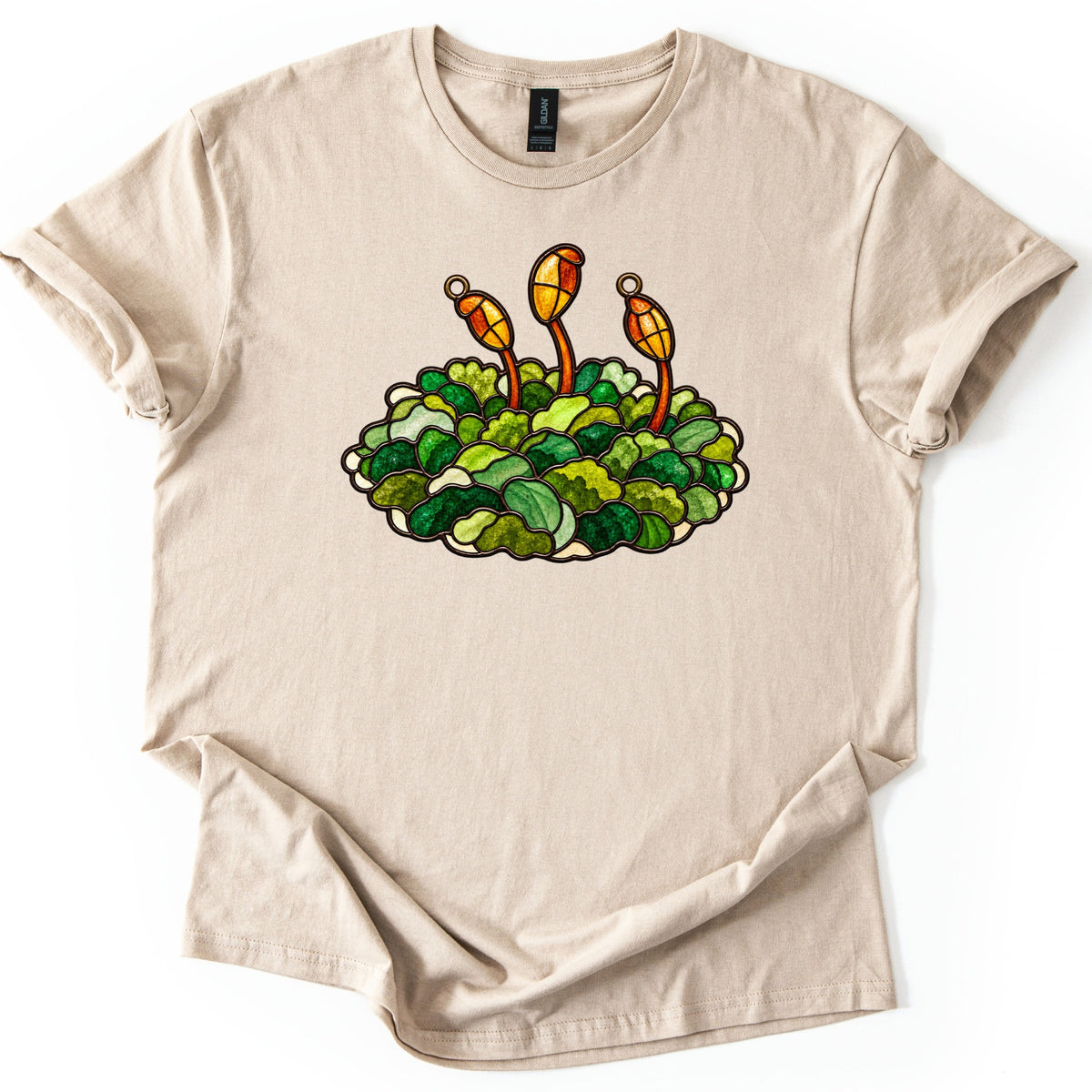Stained Glass Moss Comfort Colors T-shirt in Sand, laid flat. A stained glass style mound of green moss with three orange and yellow spore capsules on thin stalks rising from it, with no words. The shirt has rolled sleeves and lies on a white background.
