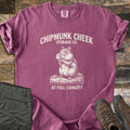 Chipmunk Cheek Storage Co Comfort Colors T-shirt in Berry, laid flat. Cream print of a chipmunk with full cheeks sitting on a log, under the words Chipmunk Cheek Storage Co. and above At Full Capacity. Rolled sleeves, on weathered wood with olive pants and brown hiking boots.