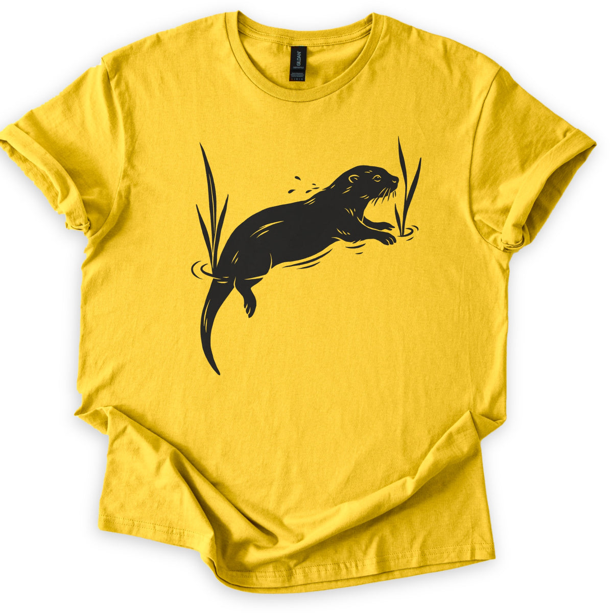 Swimming Otter Comfort Colors T-shirt in Daisy, laid flat. A black linocut-style otter swims through rippling water between tall reeds, with droplets above its head. No words are printed. The sleeves are cuffed and the shirt lies on a white background.