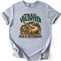 Trail Volunteer Paid in Switchbacks Comfort Colors T-shirt in Sport Grey, laid flat. Printed art shows a pickaxe resting in red dirt beside a winding trail through rocks, grass and pine trees, under the words Trail Volunteer and above Paid in Switchbacks. Sleeves are cuffed on a white background.