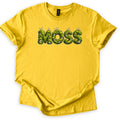Moss Comfort Colors T-shirt in Daisy, laid flat. The word MOSS is printed across the chest in puffy letters made of green moss with gray stones and thin sprouting stalks on top. The shirt has rolled sleeves and lies on a white background.