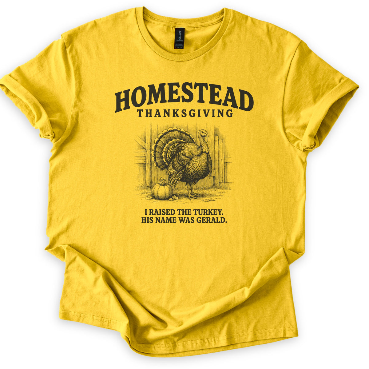 Homestead Thanksgiving Comfort Colors T-shirt in Daisy, laid flat. Black ink sketch of a fanned-tail turkey beside a pumpkin by a wooden barn, under arched Homestead Thanksgiving and above I Raised the Turkey. His Name Was Gerald. Rolled sleeves, white background.