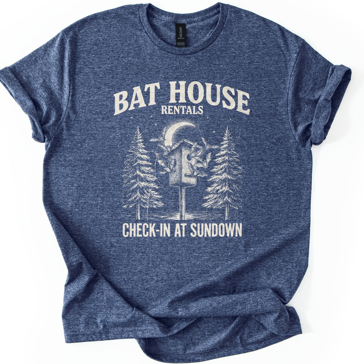Bat House Rentals Comfort Colors T-shirt in Heather Navy, laid flat. Cream text reads Bat House Rentals above a sketch of bats circling a wooden bat house on a post under a crescent moon between two pine trees, with Check-In at Sundown below. Sleeves cuffed, on white.