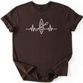 Kayak Heartbeat Comfort Colors T-shirt in Dark Chocolate, laid flat. A cream line drawing of a kayak seen from above, with a paddle across it, sits in the middle of a heartbeat line across the chest. No words are printed. The shirt lies on a white surface with rolled sleeves.