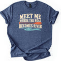 Meet Me Where the Road Becomes River Comfort Colors T-shirt in Heather Navy, laid flat. Cream text reads Meet Me Where the Road Becomes River, with an orange canoe paddle between the lines and a wavy turquoise river below. The shirt has rolled sleeves and lies on a white background.