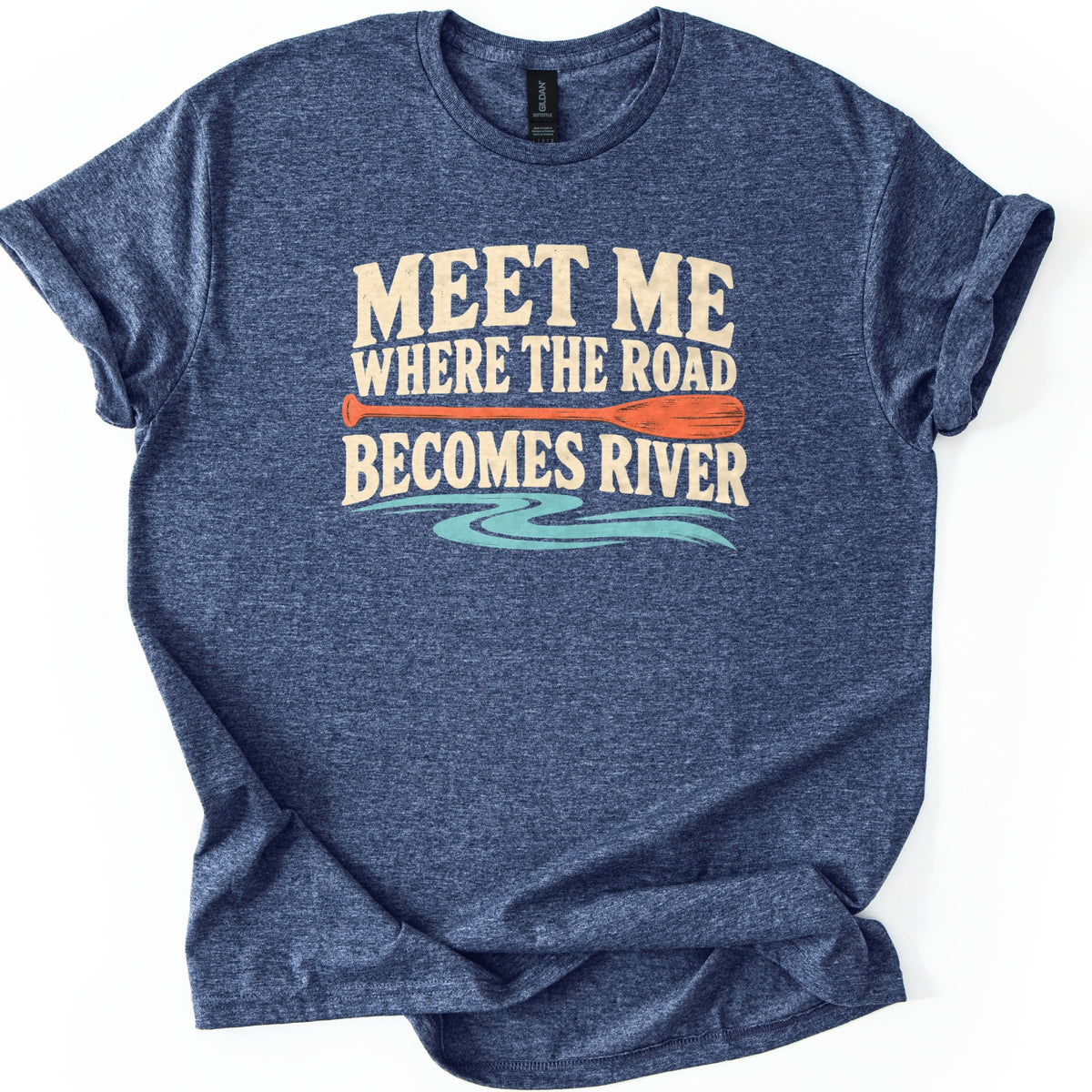 Meet Me Where the Road Becomes River Comfort Colors T-shirt in Heather Navy, laid flat. Cream text reads Meet Me Where the Road Becomes River, with an orange canoe paddle between the lines and a wavy turquoise river below. The shirt has rolled sleeves and lies on a white background.