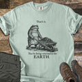 Toad Compost Comfort Colors T-shirt in Bay, laid flat. A black-ink toad in an apron pushes a wheelbarrow of compost between the words That's it. and You're being returned to the EARTH. Folded olive pants and brown hiking boots lie beside it on weathered wood.