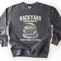 Backyard Smokehouse Comfort Colors crewneck sweatshirt in Pepper, laid flat. Large words Backyard Smokehouse sit above a sketch of a barrel smoker with a turkey on the grate, smoke rising, and a folding chair beside it, over the words Ready When It's Ready. Shown on a white background.