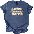 Headwinds Build Character I Have Enough Comfort Colors T-shirt in Heather Navy, laid flat. Cream lettering reads HEADWINDS, BUILD CHARACTER, I HAVE ENOUGH, with teal wave swirls and an orange kayak paddle between the lines. The shirt has rolled sleeves on a white background.