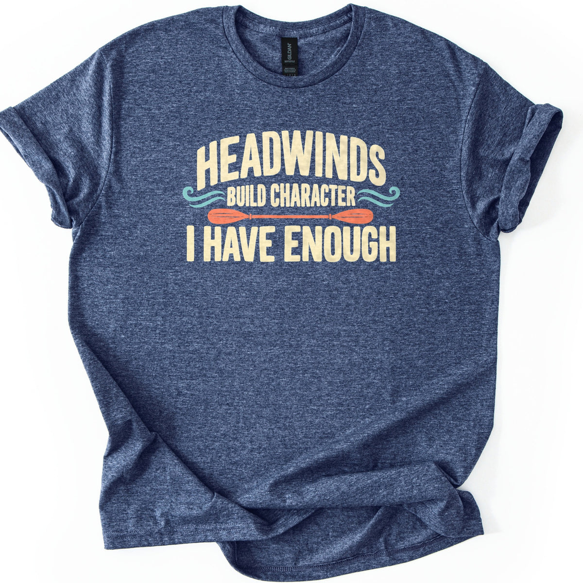 Headwinds Build Character I Have Enough Comfort Colors T-shirt in Heather Navy, laid flat. Cream lettering reads HEADWINDS, BUILD CHARACTER, I HAVE ENOUGH, with teal wave swirls and an orange kayak paddle between the lines. The shirt has rolled sleeves on a white background.
