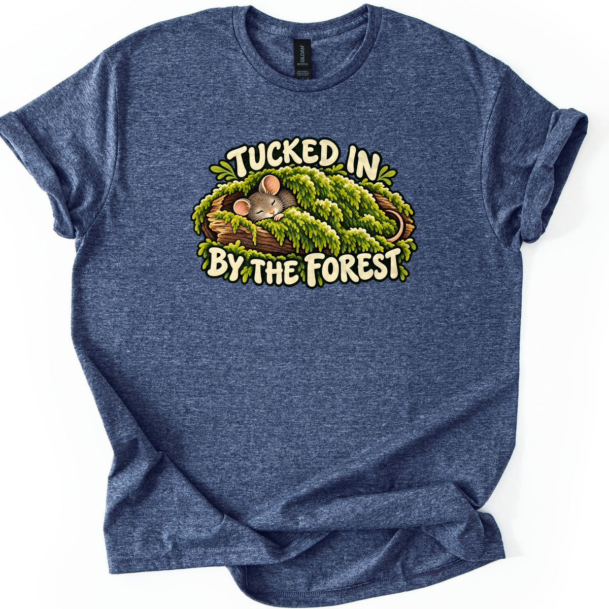 Tucked in by the Forest Comfort Colors T-shirt in Heather Navy, laid flat. A sleeping gray mouse with pink ears lies under a blanket of green moss in a hollow log, between cream words reading Tucked in By the Forest. The shirt has rolled sleeves on a white background.