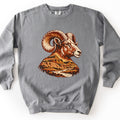 Bighorn Badlands Comfort Colors crewneck sweatshirt in Grey, laid flat. A woodcut-style bighorn ram head with curled horns, in rust, brown and cream, faces right; its chest becomes a badlands scene of layered buttes and a winding river. No words. Set on a white surface.