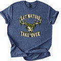 Let Nature Take Over Comfort Colors T-shirt in Heather Navy, laid flat. A cream deer skull with antlers draped in green moss sits between the words Let Nature arched above and Take Over below, in cream lettering. The sleeves are rolled on a plain white background.
