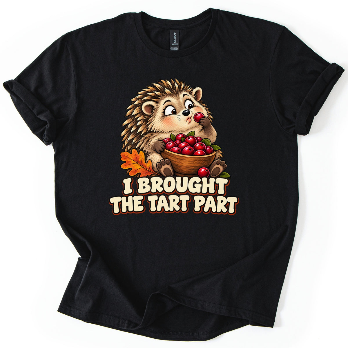I Brought the Tart Part Comfort Colors T-shirt in Black, laid flat. A cartoon hedgehog nibbles a cranberry while holding a wooden bowl full of cranberries next to an orange oak leaf, above the words I Brought the Tart Part. The sleeves are cuffed on a white background.