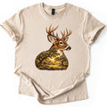Whitetail Oak Grove Comfort Colors T-shirt in Sand, laid flat. A whitetail buck with branching antlers faces right, its neck and chest filled with a painted grove of oak trees and a meadow in golden sunlight. No words are printed. Cuffed sleeves on a white surface.