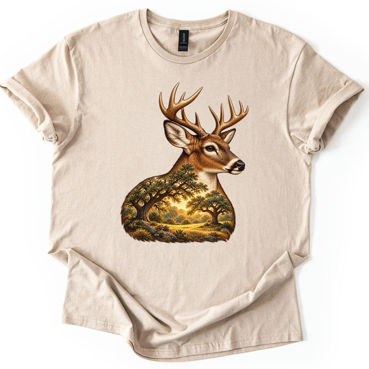Whitetail Oak Grove Comfort Colors T-shirt in Sand, laid flat. A whitetail buck with branching antlers faces right, its neck and chest filled with a painted grove of oak trees and a meadow in golden sunlight. No words are printed. Cuffed sleeves on a white surface.