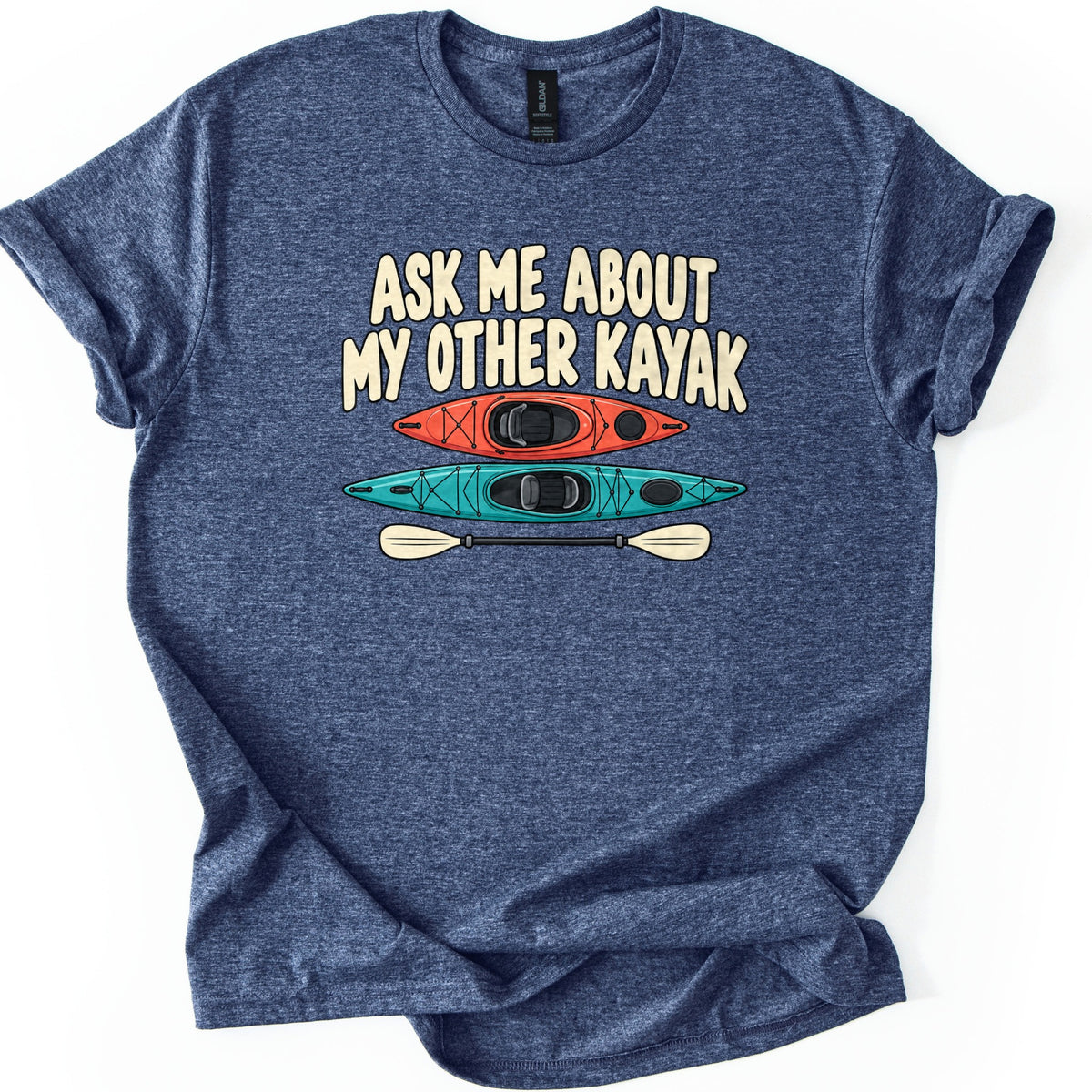Other Kayak Comfort Colors T-shirt in Heather Navy, laid flat. Cream letters read Ask Me About My Other Kayak above a top view of an orange kayak, a longer teal kayak, and a cream double-bladed paddle. The shirt has rolled sleeves on a white background.