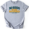 No Birds Were Bothered Comfort Colors T-shirt in Sport Grey, laid flat. Bold text reads No Birds in dark teal and Were Bothered in mustard yellow, above Clay Days in small teal letters set between two lines. The shirt has rolled sleeves on a white background.