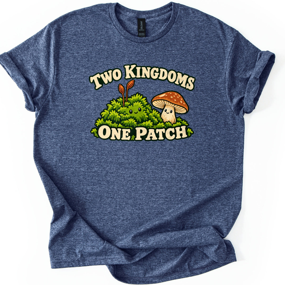 Two Kingdoms One Patch Comfort Colors T-shirt in Heather Navy, laid flat. A smiling green moss clump with two orange spore stalks sits beside a smiling spotted brown mushroom, between the words Two Kingdoms and One Patch. The sleeves are rolled on a white background.