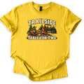 Trailside Table for Two Comfort Colors T-shirt in Daisy, laid flat. A man and woman in caps sit on a plaid picnic blanket with mugs and bread, pine trees and an off-road side-by-side behind them, between the words Trailside and Table for Two. Sleeves cuffed, on white.