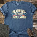 Headwinds Build Character I Have Enough Comfort Colors T-shirt in Denim, laid flat. Cream text reads Headwinds Build Character I Have Enough, with teal wave swirls and an orange kayak paddle. Sleeves rolled, on weathered wood beside olive hiking pants and brown hiking boots.