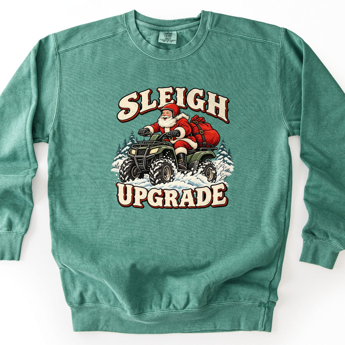 Sleigh Upgrade Comfort Colors crewneck sweatshirt in Light Green, laid flat. Santa in a red helmet rides a green ATV through snow with a red gift sack strapped behind him and pine trees around, under the words Sleigh Upgrade in cream retro letters. Shown on a white background.