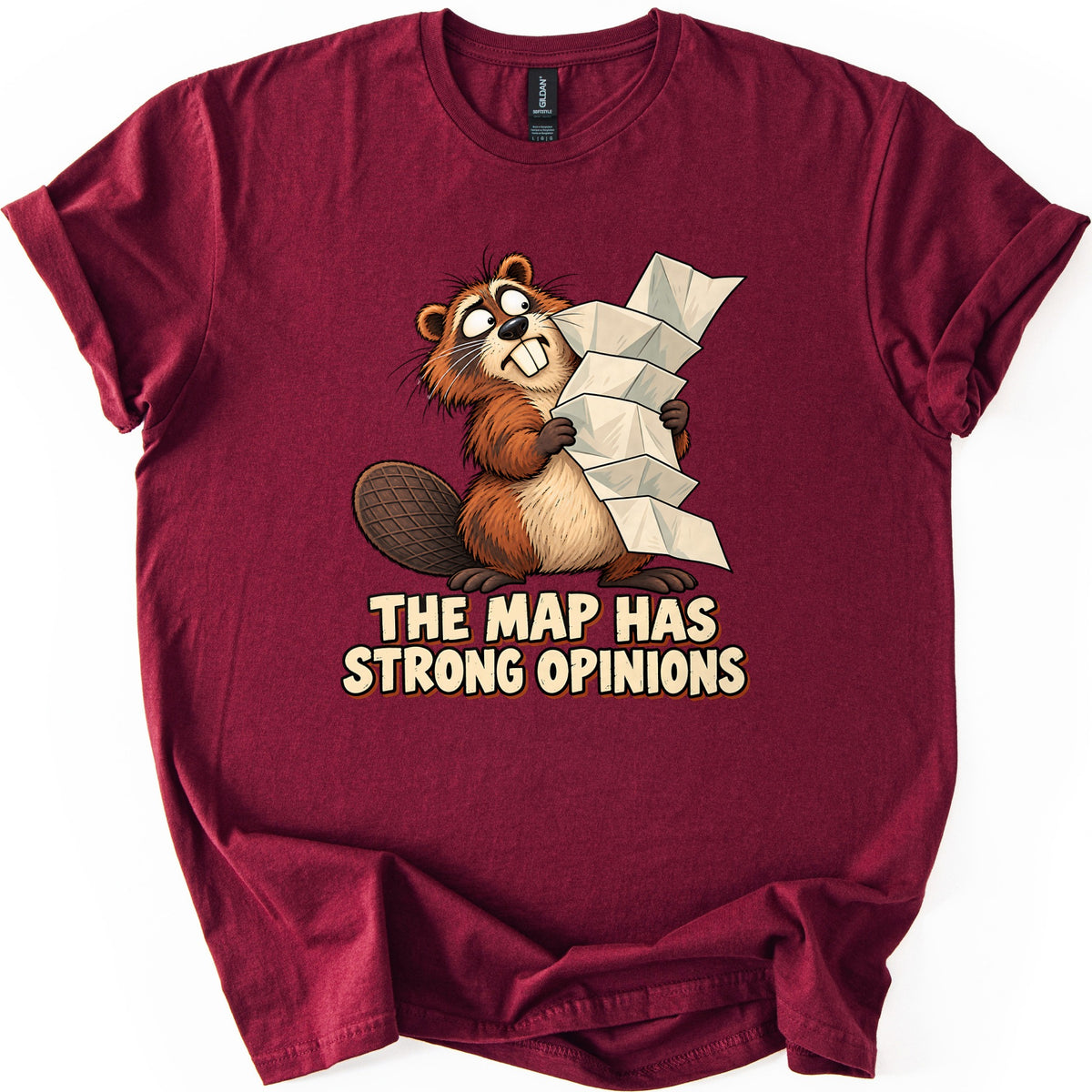 The Map Has Strong Opinions Comfort Colors T-shirt in Maroon, laid flat. A wide-eyed cartoon beaver with buck teeth clutches a tall, unfolding paper map above the words The Map Has Strong Opinions in cream lettering. The shirt has rolled sleeves on a white background.