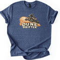Dune Drifter Comfort Colors T-shirt in Heather Navy, laid flat. A helmeted rider on an orange and black ATV kicks up orange sand above the words Dune Drifter in cream letters. The shirt has cuffed sleeves and lies on a white background.