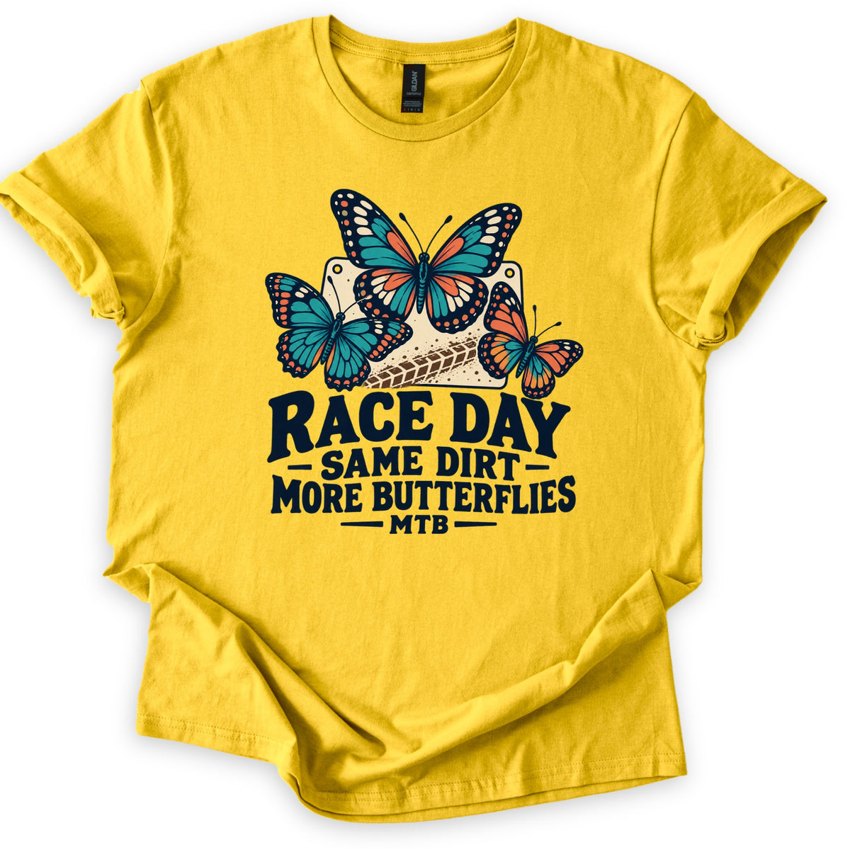 Race Day Same Dirt More Butterflies Comfort Colors T-shirt in Daisy, laid flat. Three teal and orange butterflies sit on a cream race number plate with a dirt tire track, above the words Race Day, Same Dirt, More Butterflies, MTB. The shirt lies on white with rolled sleeves.