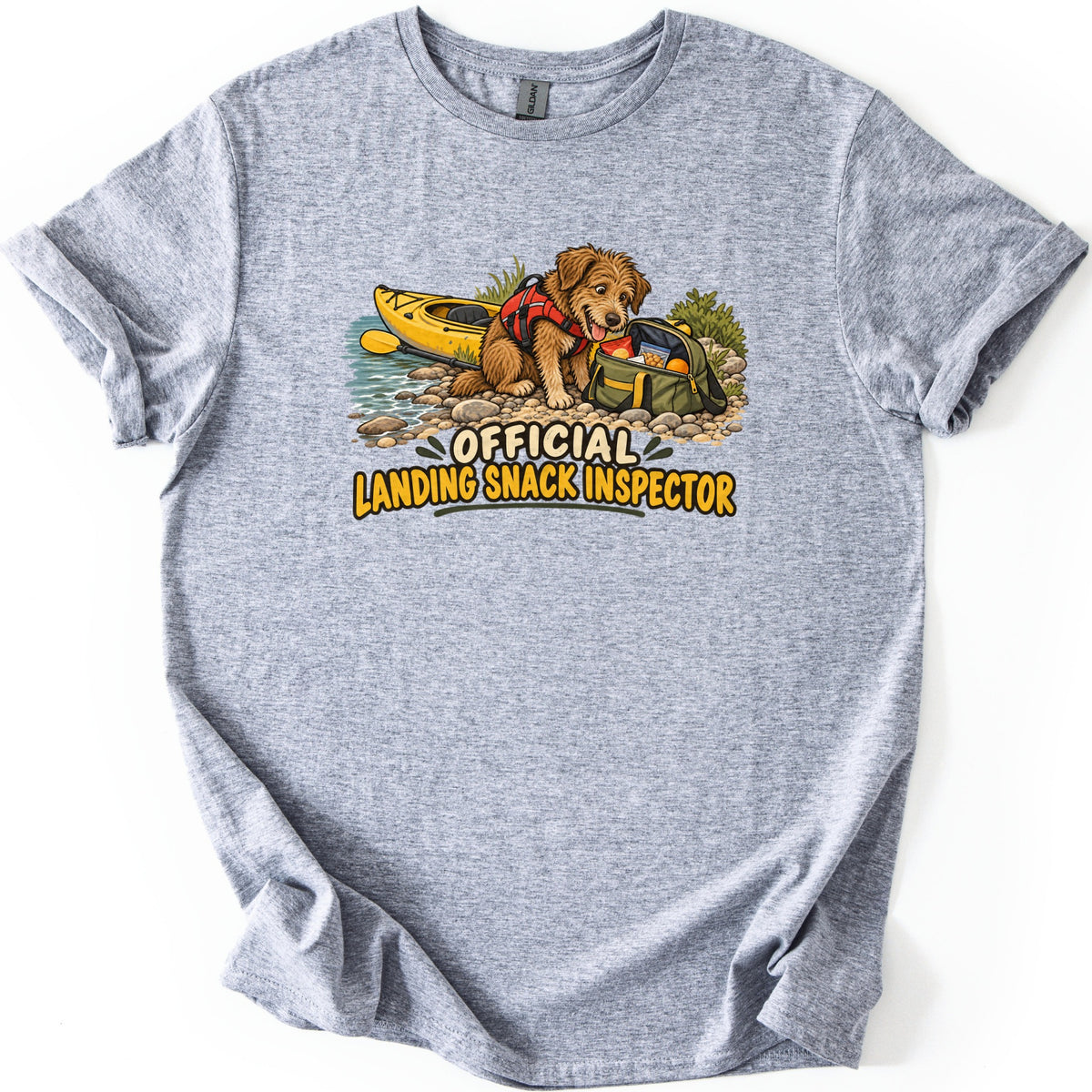 Landing Snack Inspector Comfort Colors T-shirt in Sport Grey, laid flat. A scruffy brown dog in a red life vest noses into an open green bag of snacks on a rocky riverbank by a yellow kayak, above the words Official Landing Snack Inspector. Sleeves rolled, on white.