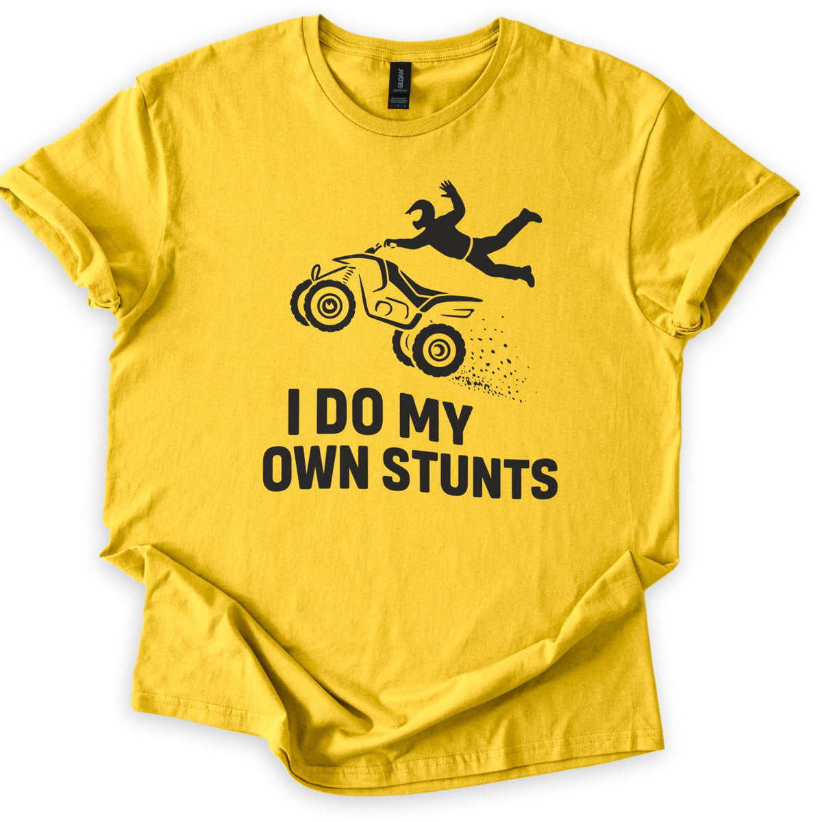 ATV Stunts Comfort Colors T-shirt in Daisy, laid flat. A black silhouette of a helmeted rider flying off the back of an ATV as it kicks up dirt, above the words I DO MY OWN STUNTS. The shirt lies on a white background with its sleeves cuffed.