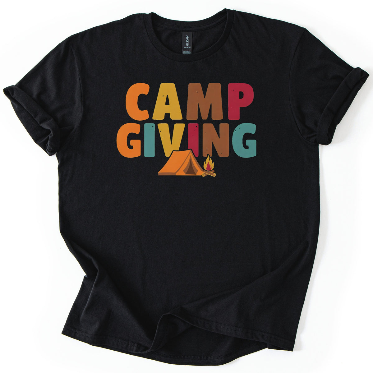 Campgiving Comfort Colors T-shirt in Black, laid flat. The words Camp Giving in large orange, yellow, brown, red and teal letters, with an orange tent and a small campfire on logs below. The shirt has rolled sleeves and lies on a white background.
